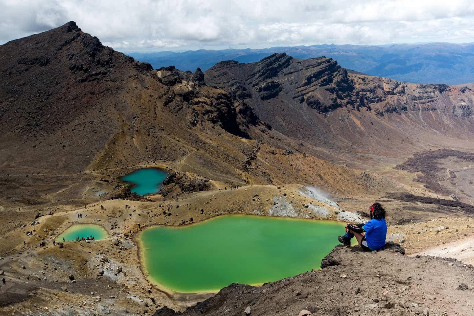 shuttle-service-for-tongariro-alpine-crossing-tongariro-expeditions-feature-1 | Must Do New Zealand | Must Do New Zealand Tramper sitting looking over Green lake on Tongariro Alpine Crossing