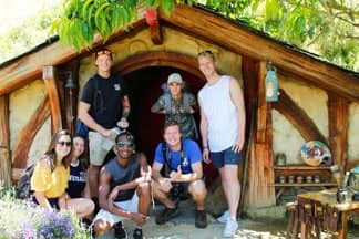 Group of backpackers crouching in front of Hobbit House at Hobbiton Film set, Matamata | Must Do New Zealand Group of backpackers crouching in front of Hobbit House at Hobbiton Film set, Matamata