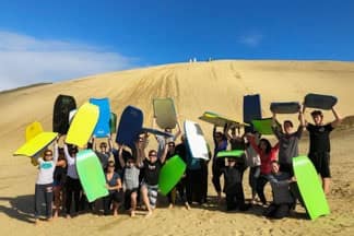 Group of backpackers sand boarding at Te Paki sand dunes, Cape Reinga | Must Do New Zealand Group of backpackers sand boarding at Te Paki sand dunes, Cape Reinga